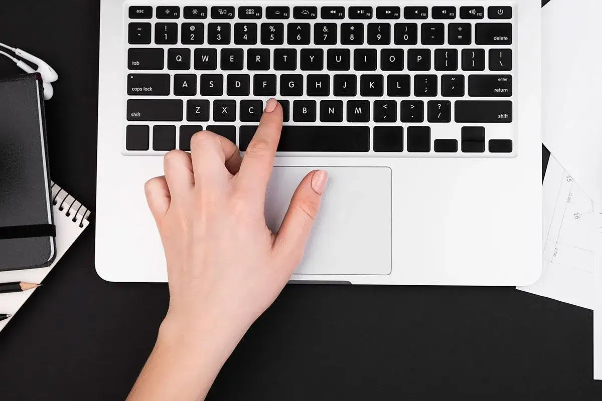 Dłoń naciska klawisz "C" na klawiaturze laptopa, co może być przyczyną, dlaczego nie działa klawiatura w laptopie.