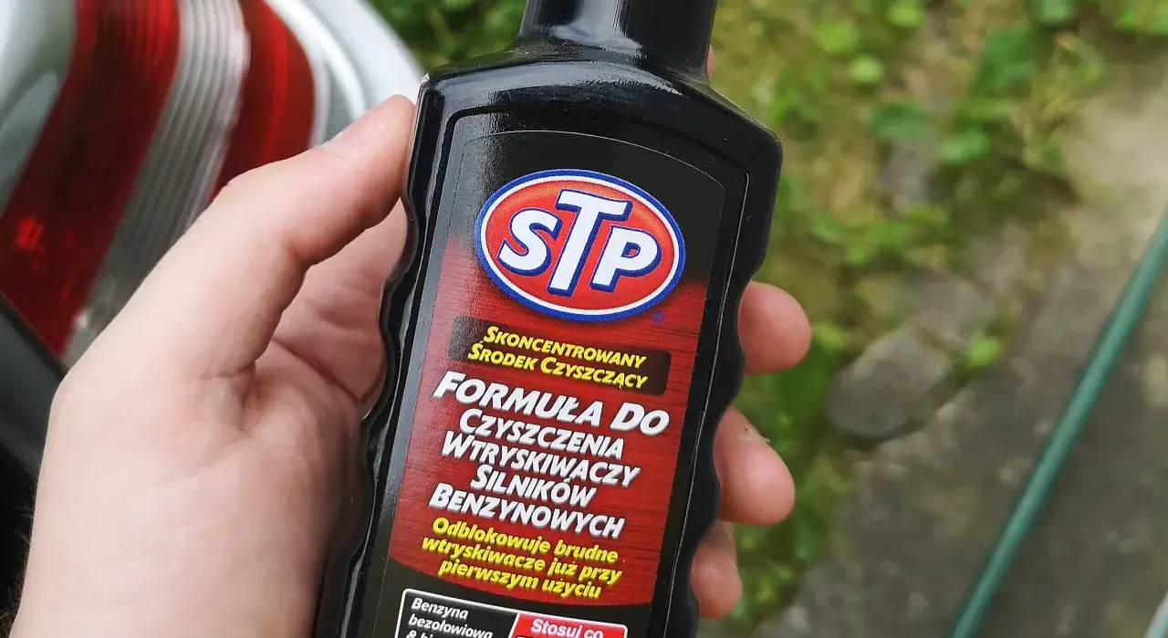 Dłoń trzyma butelkę STP z płynem do czyszczenia wtryskiwaczy. Skoncentrowana formuła odblokowuje brudne wtryskiwacze.