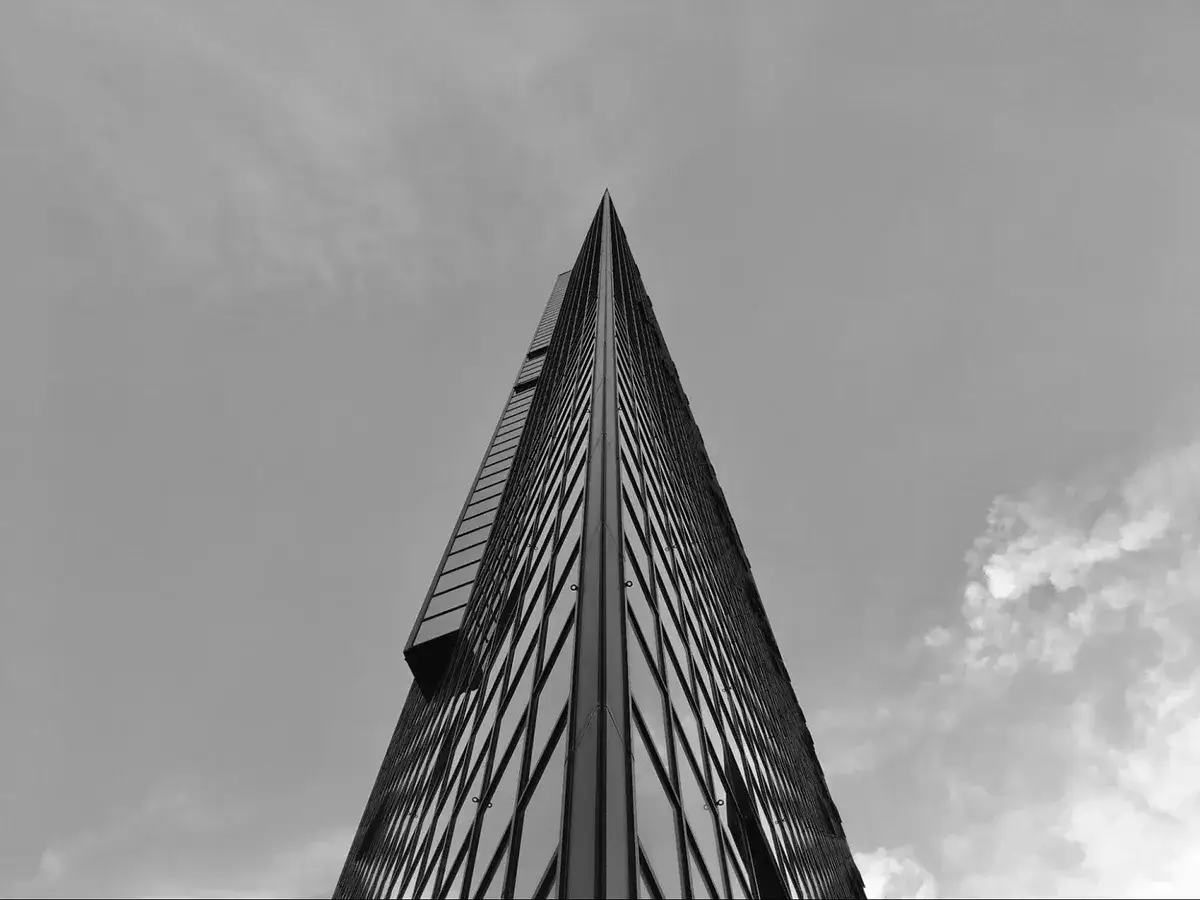 Minimalistyczne fotografowanie architektury. Ostry szczyt wieżowca przecina niebo, odbijając chmury w szklanej fasadzie.