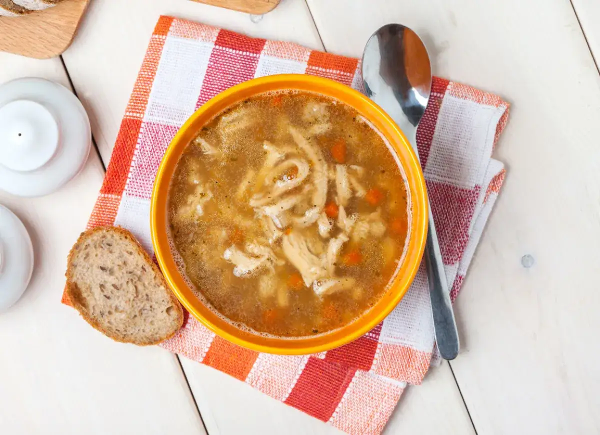 Aromaticzne flaki po zamojsku w pomarańczowej misce, obok kromka chleba i łyżka. Pyszne danie gotowe do spożycia.