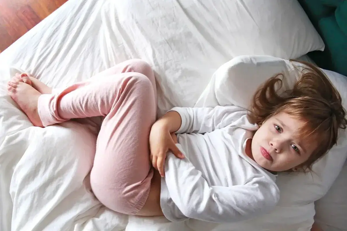 Dziewczynka w piżamie leży na łóżku, trzymając się za brzuch.