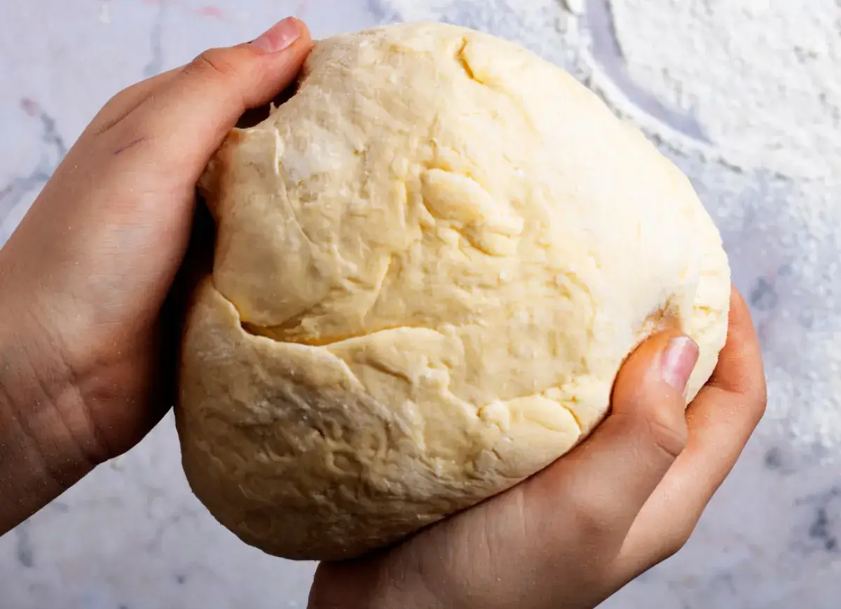 Dłonie formują puszyste ciasto drożdżowe na suchych drożdżach, gotowe do pieczenia.
