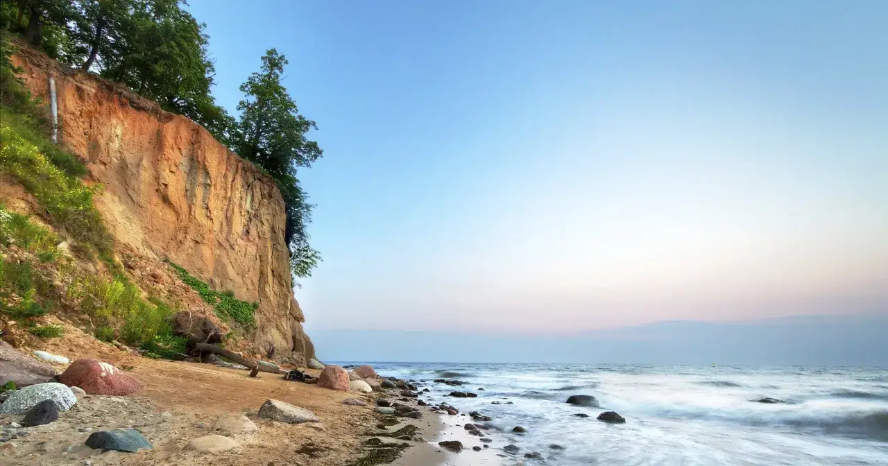 Piękna linia brzegowa Bałtyku w Polsce z klifem porośniętym drzewami i piaszczystą plażą.