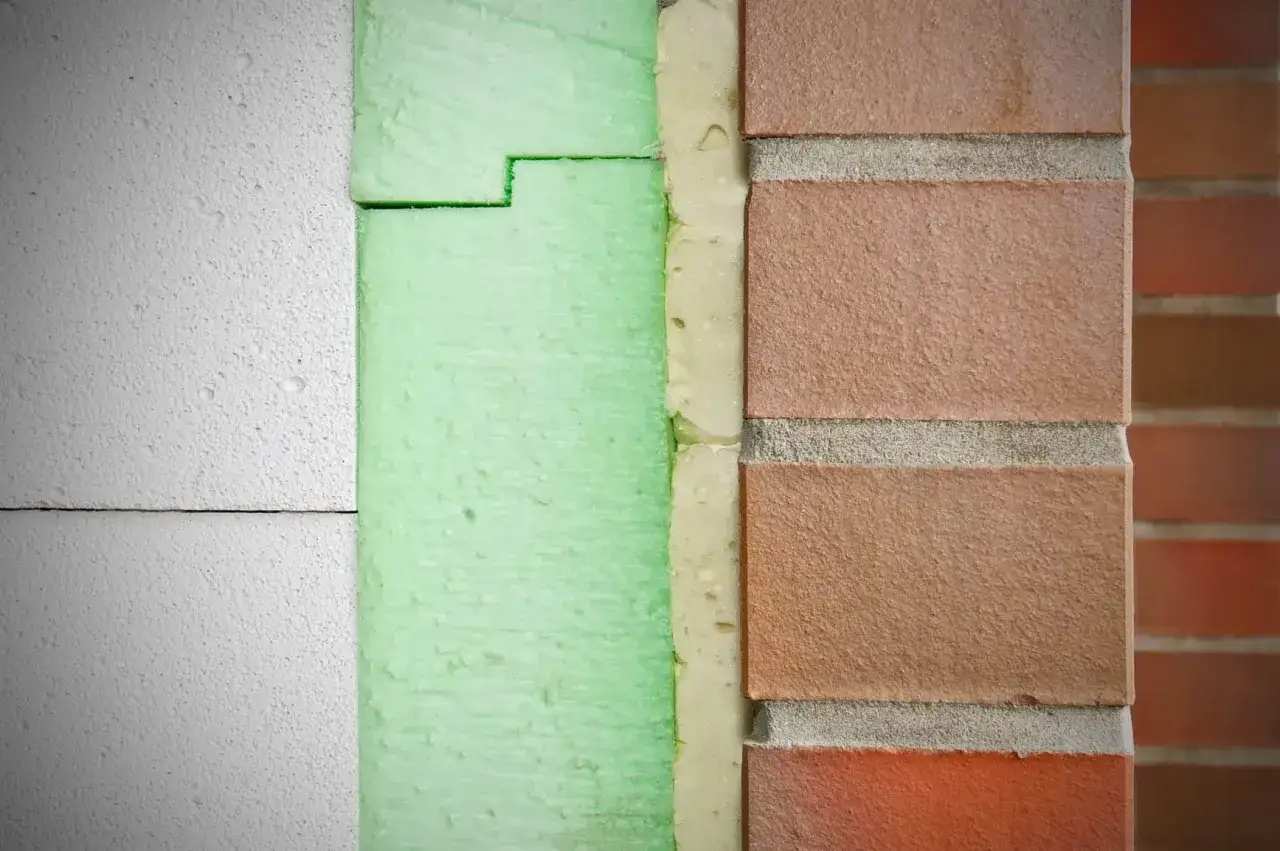 Warstwowa izolacja budynku: biały styrodur, zielona pianka, cegła. Dowiedz się, czym malować styrodur, by zabezpieczyć go przed warunkami atmosferycznymi.