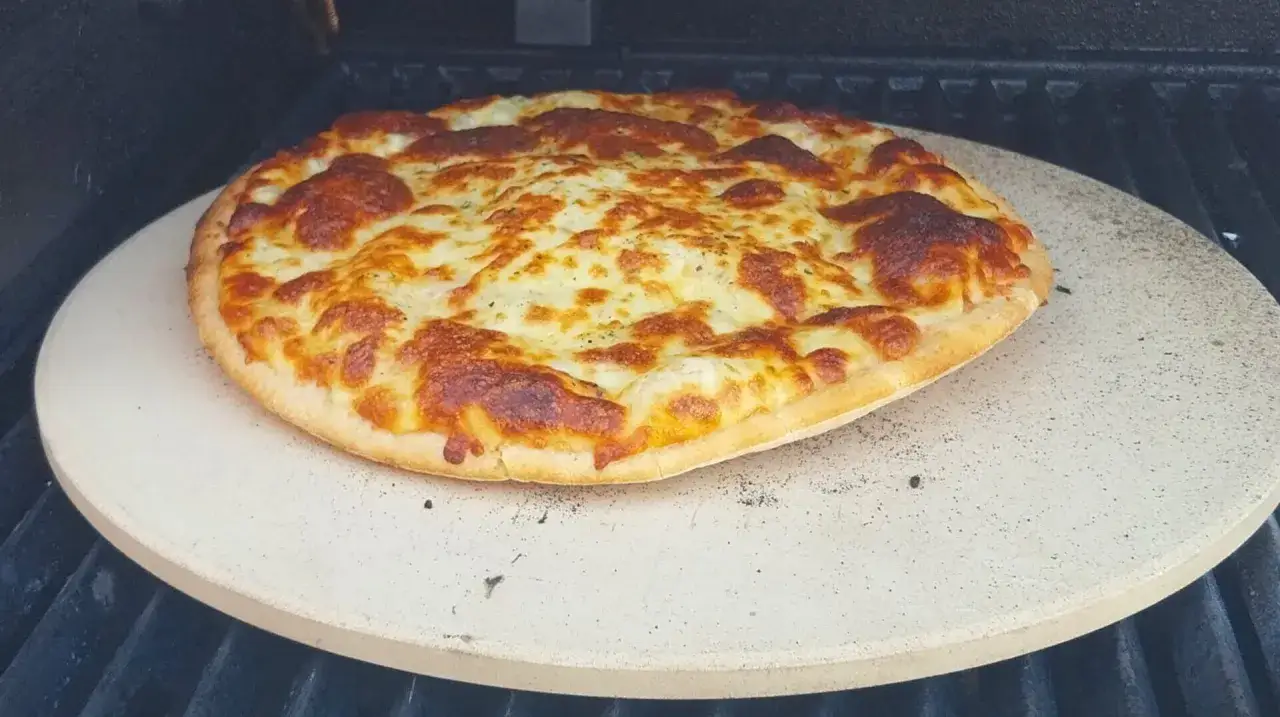 Upieczona pizza z roztopionym serem na kamieniu do pizzy na grillu.