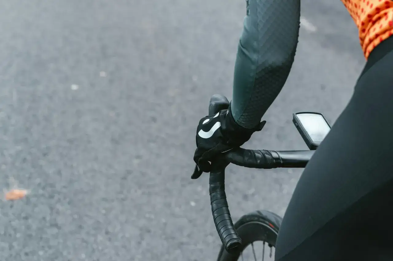 Rowerzysta w rękawiczkach z logo, trzymający kierownicę szosową. Kluczowe jest, jak dobrać szerokość kierownicy szosowej dla komfortu.