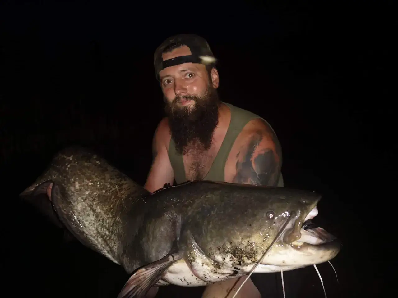 Mężczyzna w czapce z daszkiem trzyma dużego suma.