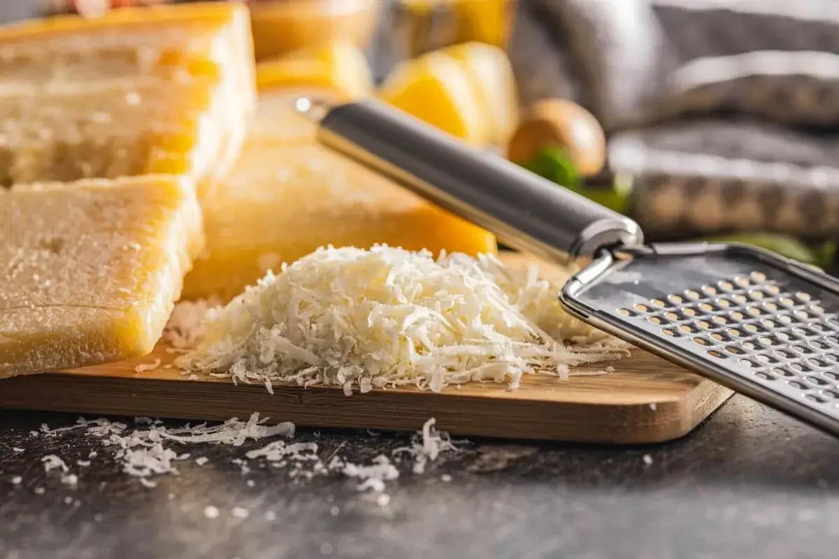Stos tartego parmezanu i kawałki sera na desce, obok tarka. Idealny składnik do każdej potrawy.