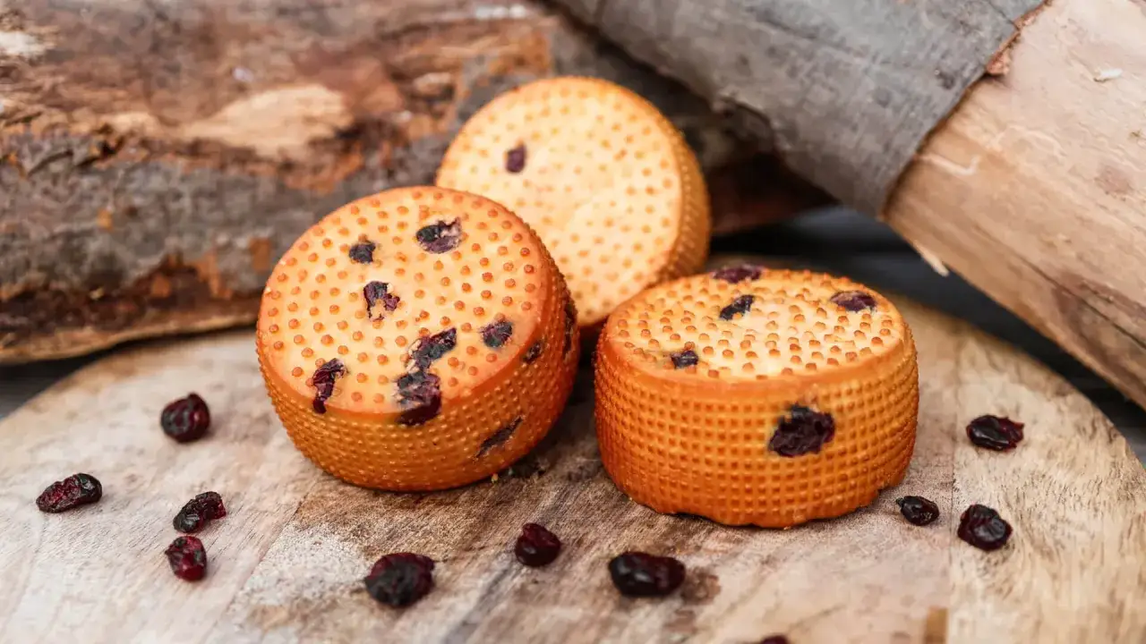 Trzy okrągłe, pomarańczowe sery z suszoną żurawiną, przypominające wyglądem oscypek z bacówki.