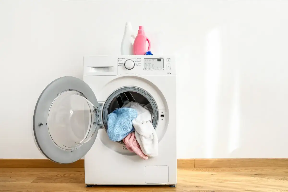 Pranie parowe w pralce: biała pralka z otwartymi drzwiczkami, w środku kolorowe ręczniki. Na górze dwie butelki z płynem do prania.