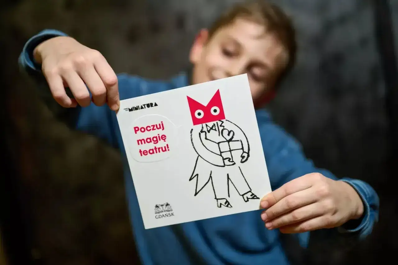 Chłopiec trzyma kartkę z napisem "Poczuj magię teatru!". To zaproszenie na spektakl, idealne bilety do teatru dla dzieci.