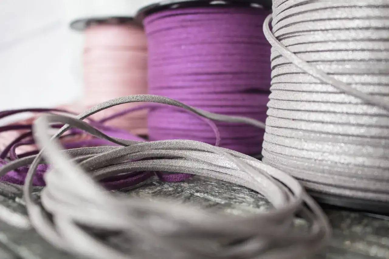 Srebrny, fioletowy i różowy rzemień do wiązania, zwinięty na szpulach, tworzy kolorową kompozycję.