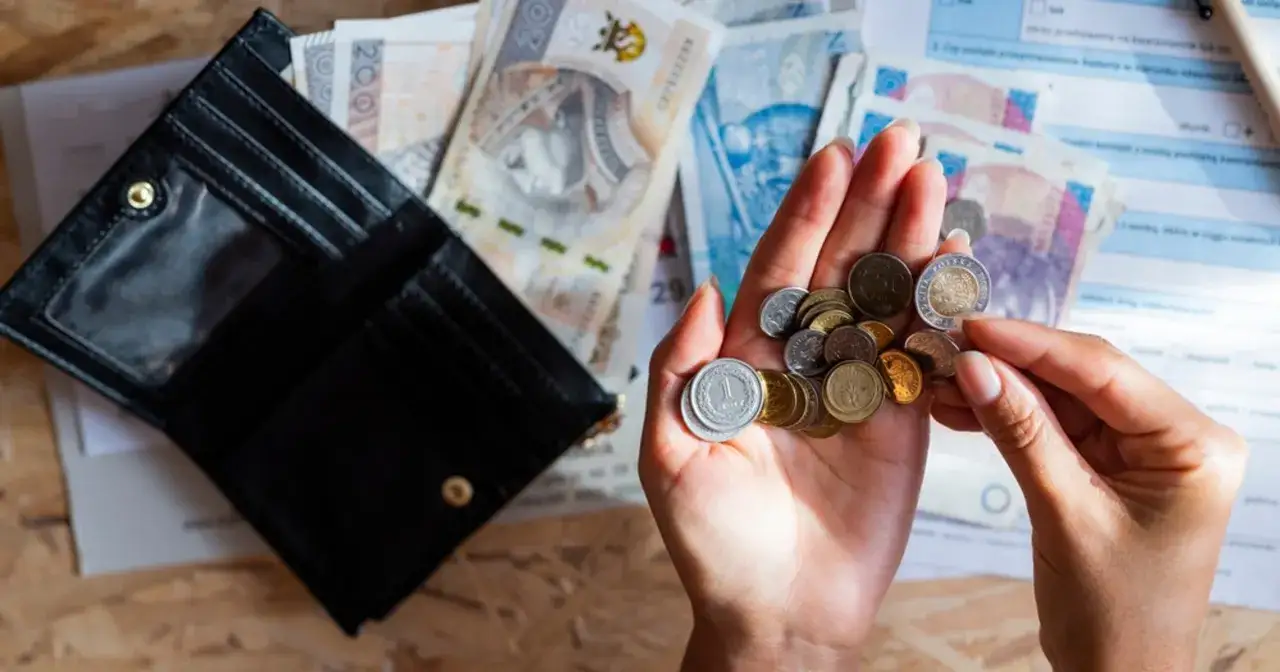 Otwarty portfel, polskie banknoty i monety w dłoni na tle dokumentów.