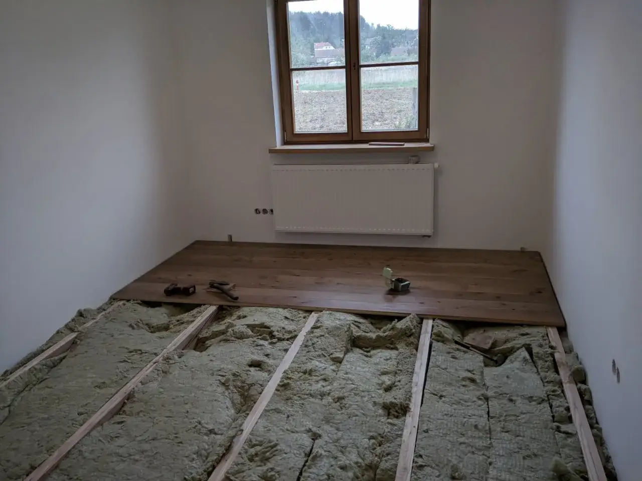 Podłoga na legarach na poddaszu, w trakcie montażu drewnianych desek. Widoczna wełna mineralna izolacyjna.