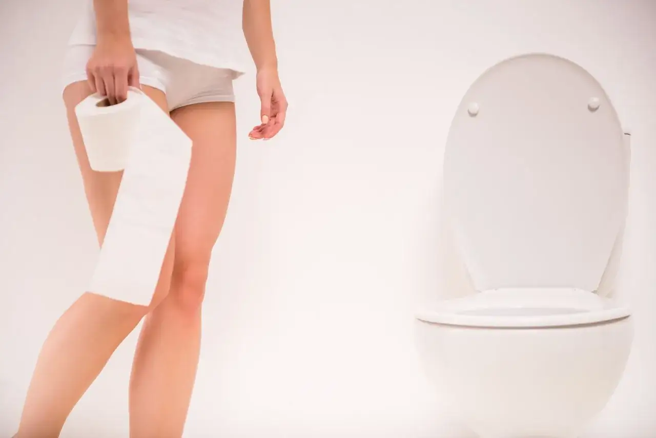 Kobieta z rolką papieru toaletowego obok sedesu. Szuka leków na częste oddawanie moczu w nocy.