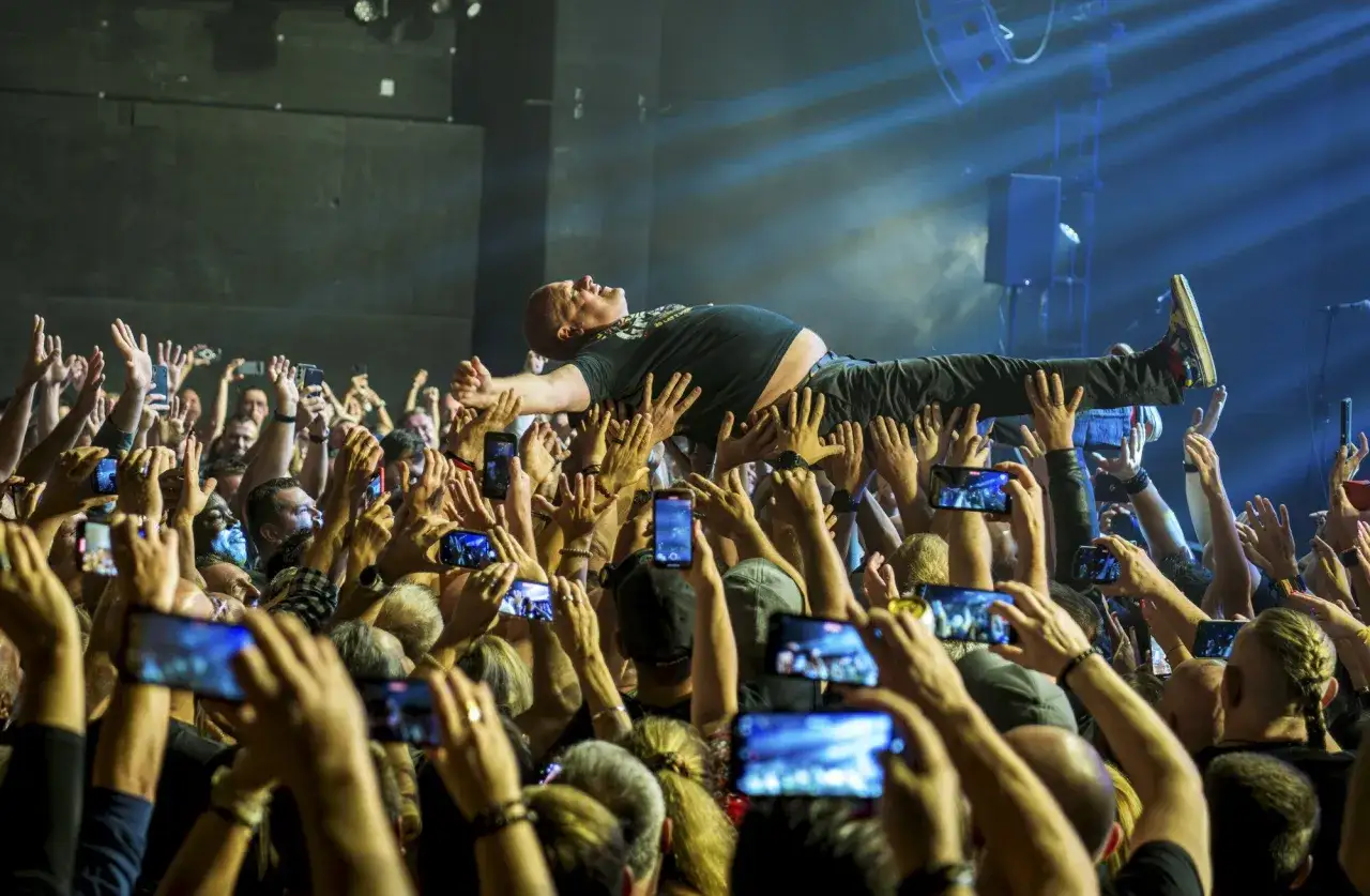 Kult w Arahji: wokalista zespołu niesiony przez tłum, fani nagrywają koncert telefonami.