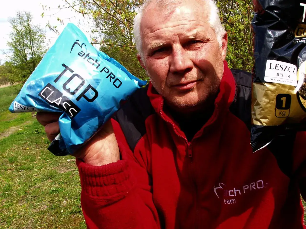 Mężczyzna w czerwonej bluzie prezentuje zanętę Match Pro Top Class i zanętę na leszcza.