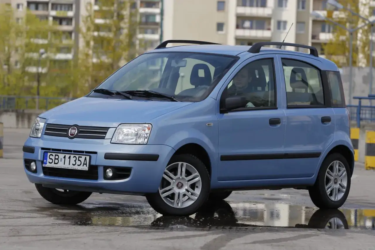 Niebieski fiat panda automat z relingami dachowymi, zaparkowany na mokrym asfalcie.