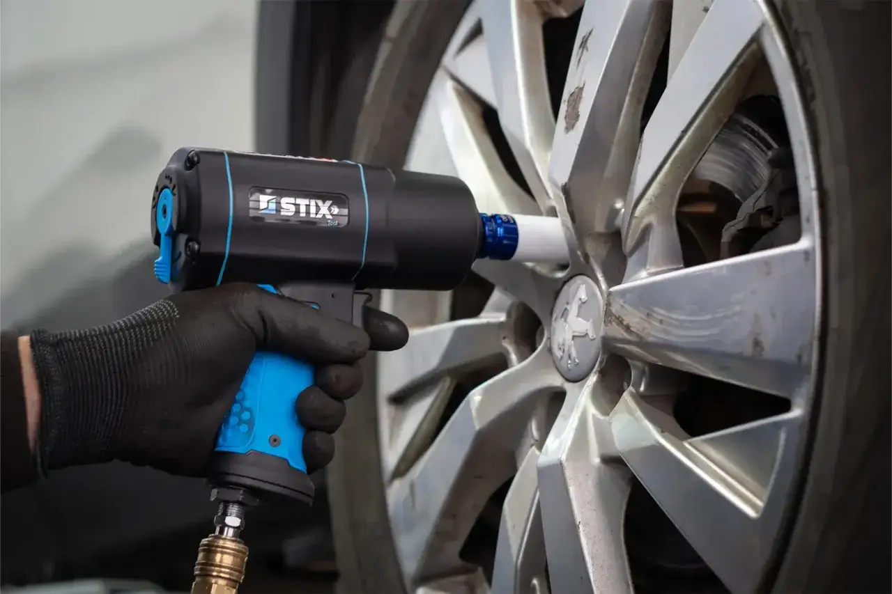 Ręka w rękawicy trzyma klucz pneumatyczny przy feldze samochodu.