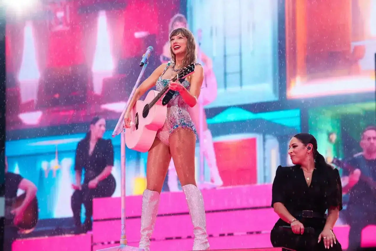 Taylor Swift, ile lat ma, na scenie z różową gitarą, w błyszczącym stroju i białych kozakach.