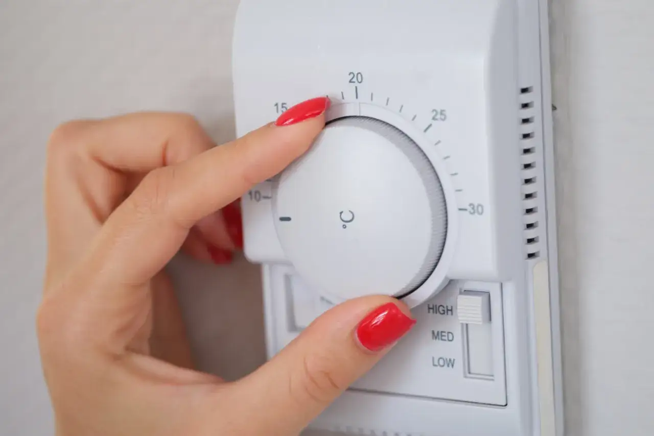 Dłoń z czerwonym lakierem reguluje termostat, ustawiając temperaturę dla elektro zaworów do CO.