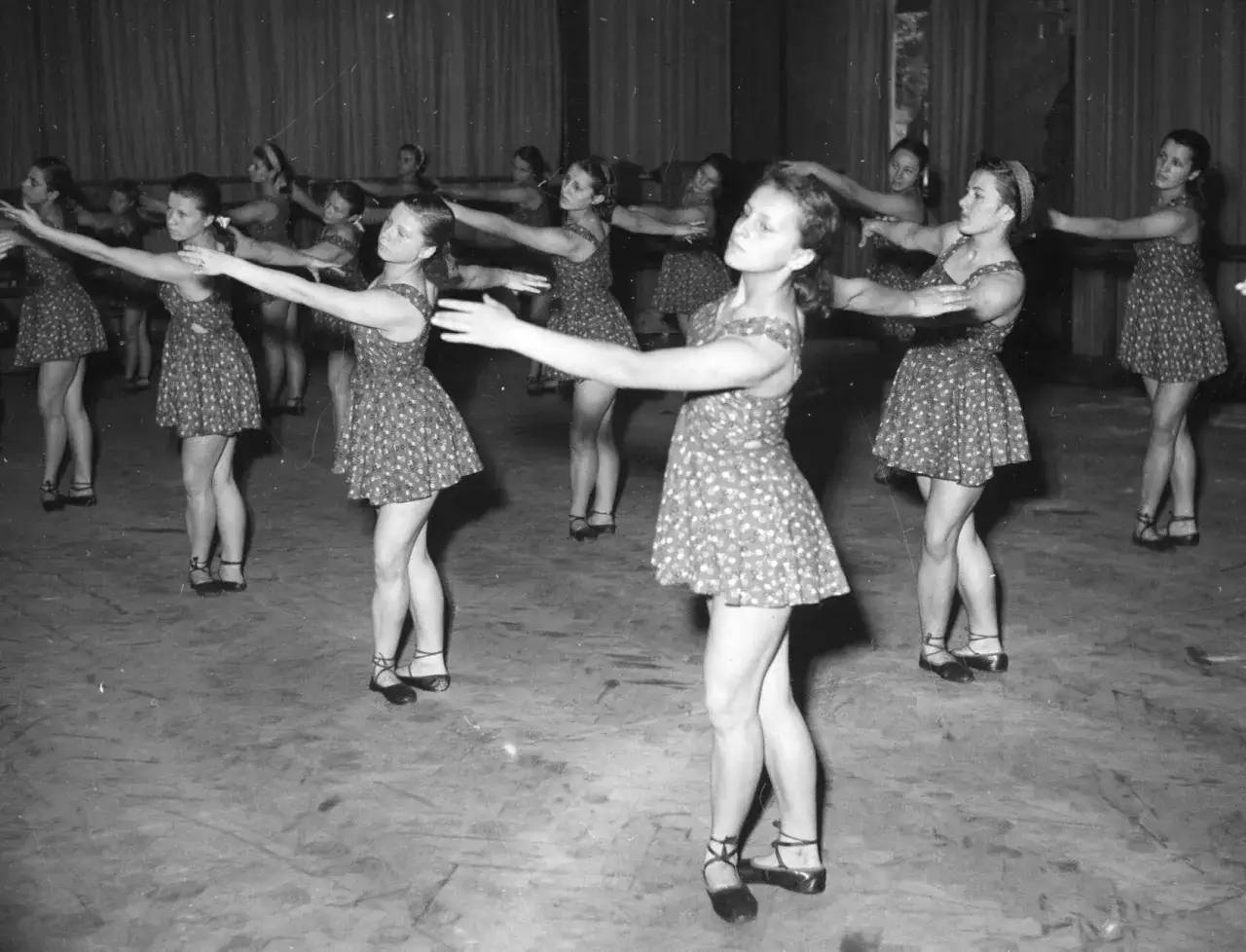 Młode tancerki w ludowych strojach ćwiczą choreografię. Ich ruchy synchronizują się z rytmem, jakby grały zespoły polskiej muzyki ludowej.