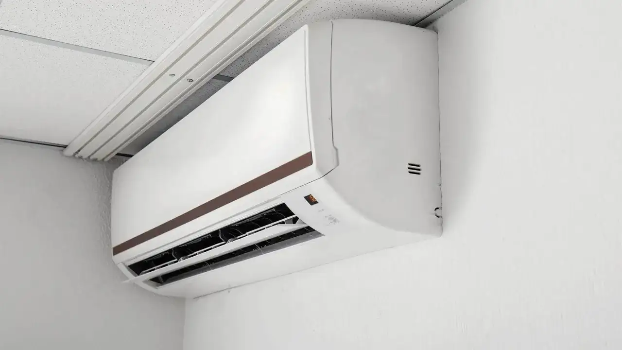 Biała jednostka klimatyzacyjna zamontowana na ścianie pod sufitem podwieszanym.