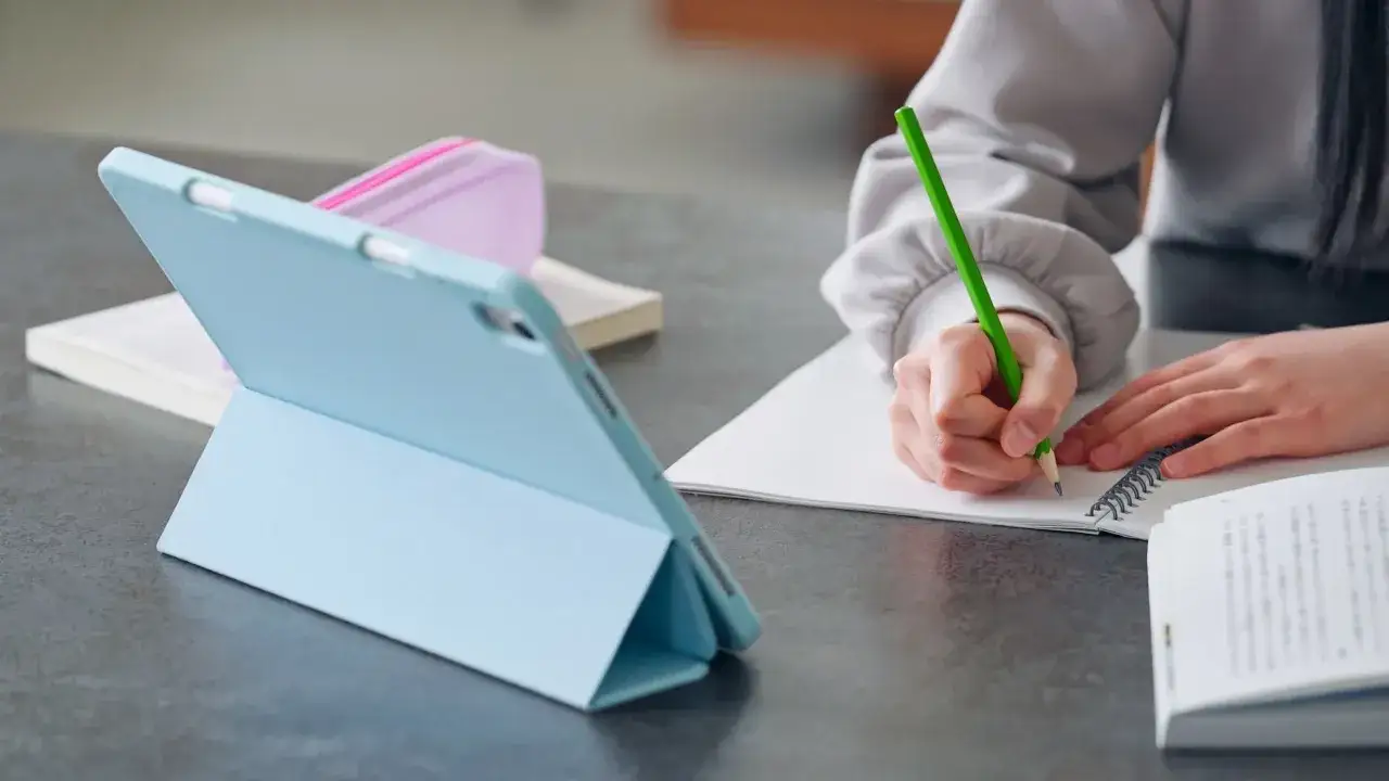 Uczeń pisze w zeszycie, korzystając z tabletu. Tak właśnie płaci się za nauczanie indywidualne w erze cyfrowej.
