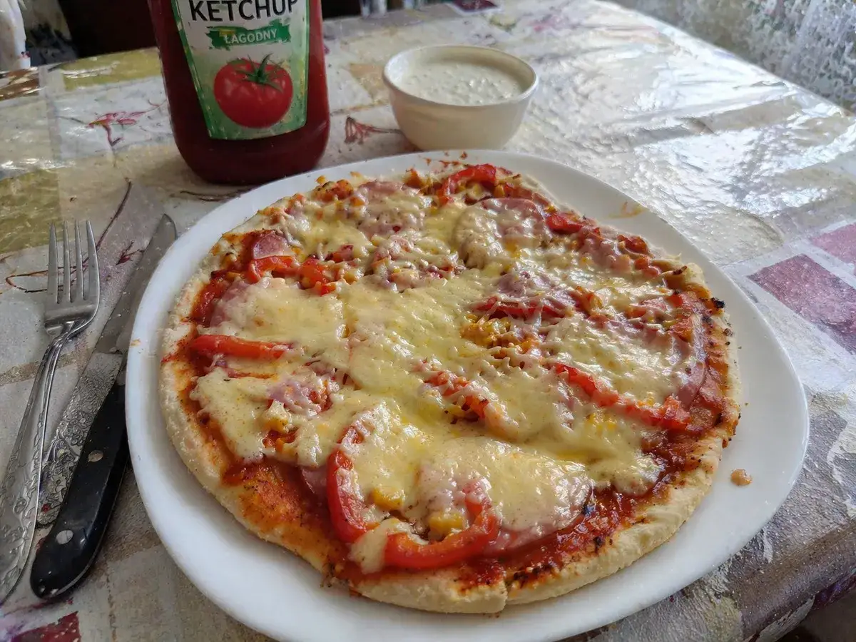 Pyszna pizza z patelni z serem, pomidorami i kukurydzą, obok ketchup i sos.