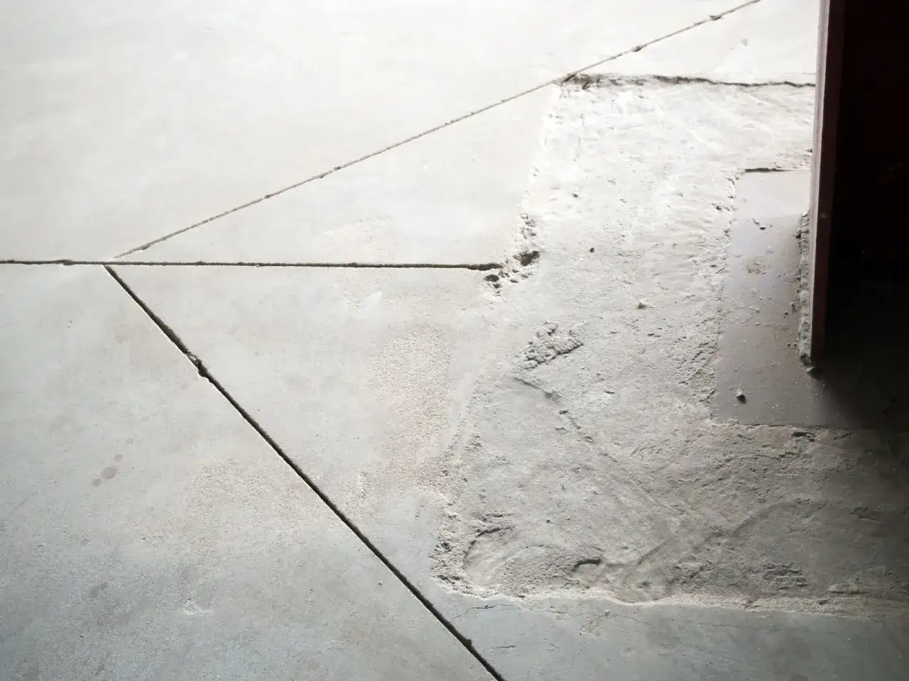 Szara posadzka z widocznymi szczelinami i ubytkami, które mogą być przykładem dylatacji.