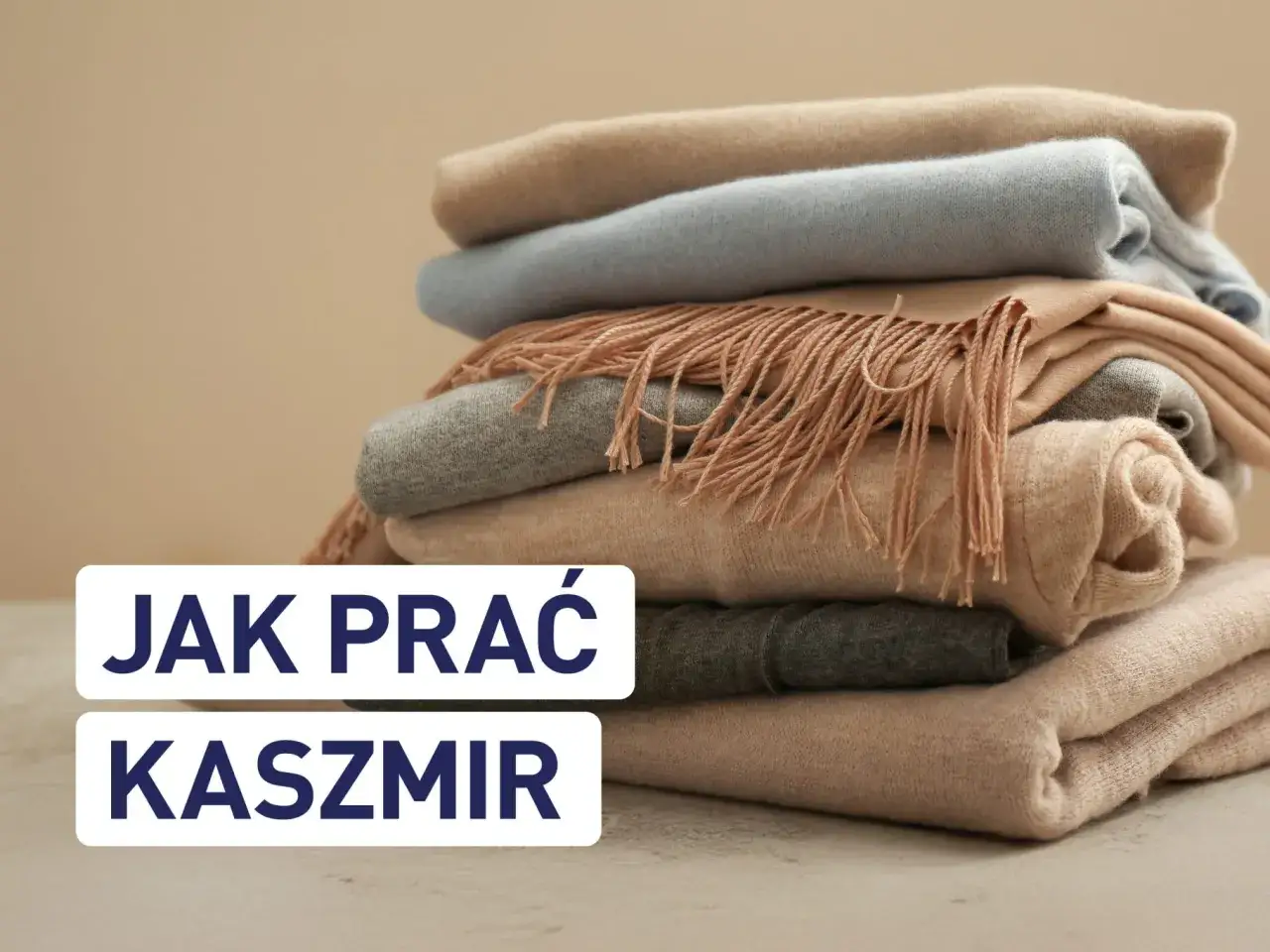 Stos miękkich, kaszmirowych szalików w pastelowych kolorach. Napis "Jak prać kaszmir" sugeruje delikatne metody pielęgnacji.