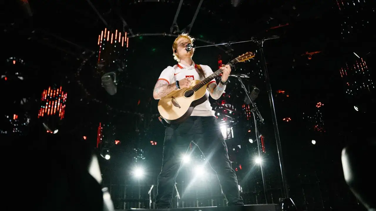Ed Sheeran gra na gitarze na scenie w białej koszulce z polskim godłem.