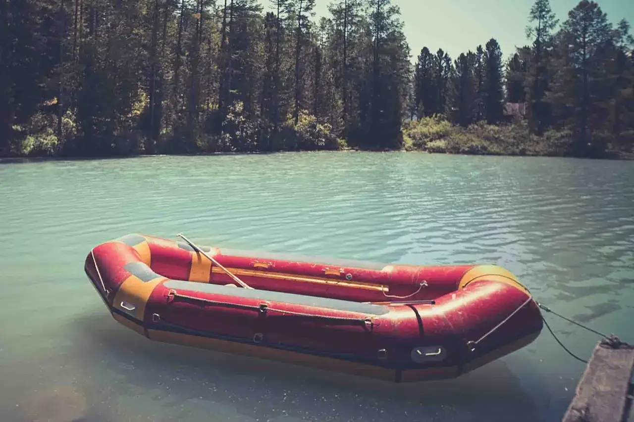 Czerwony ponton na ryby unosi się na spokojnej, turkusowej wodzie. W tle las.