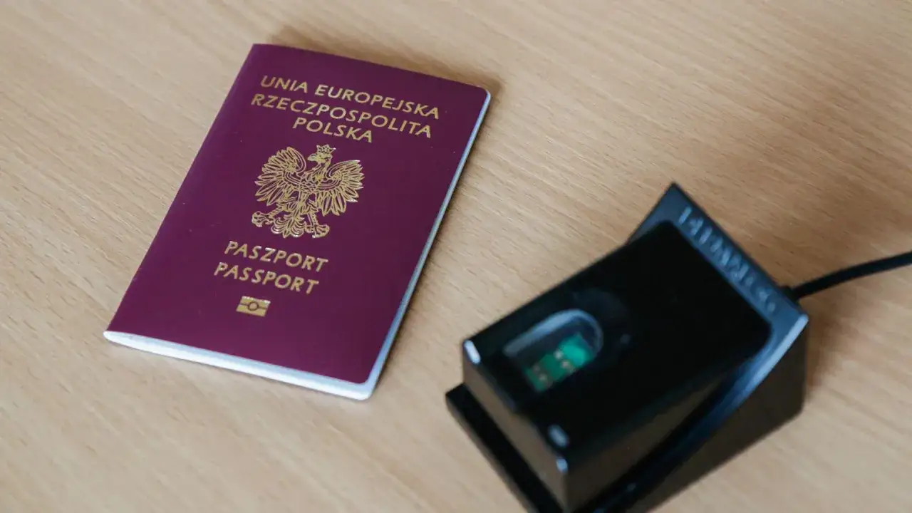 Polski paszport i czytnik linii papilarnych na drewnianym blacie.