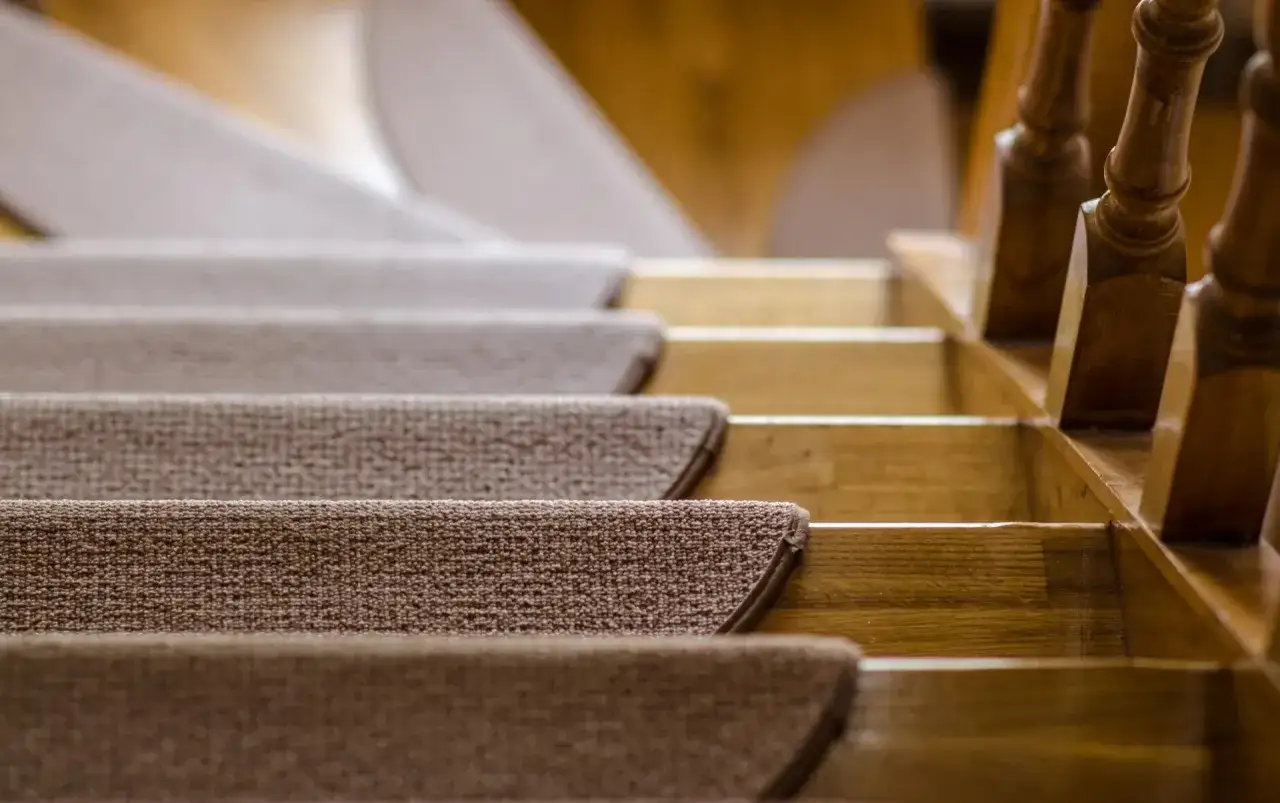 Ciepłe, brązowe schody z wykładziny prowadzą w górę, obok drewnianej balustrady.