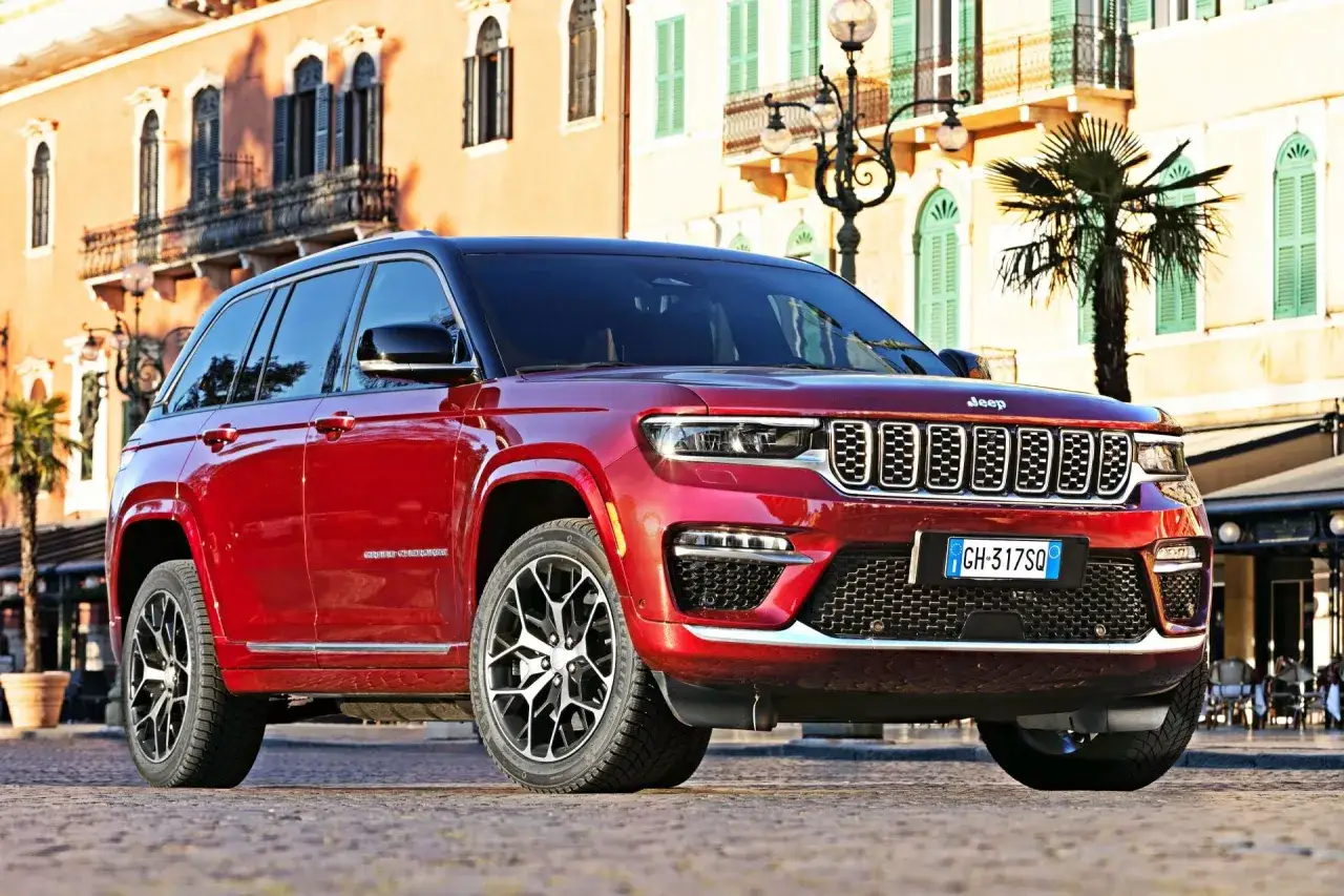 Czerwony Jeep Grand Cherokee zaparkowany na brukowanej ulicy przed budynkami z balkonami.
