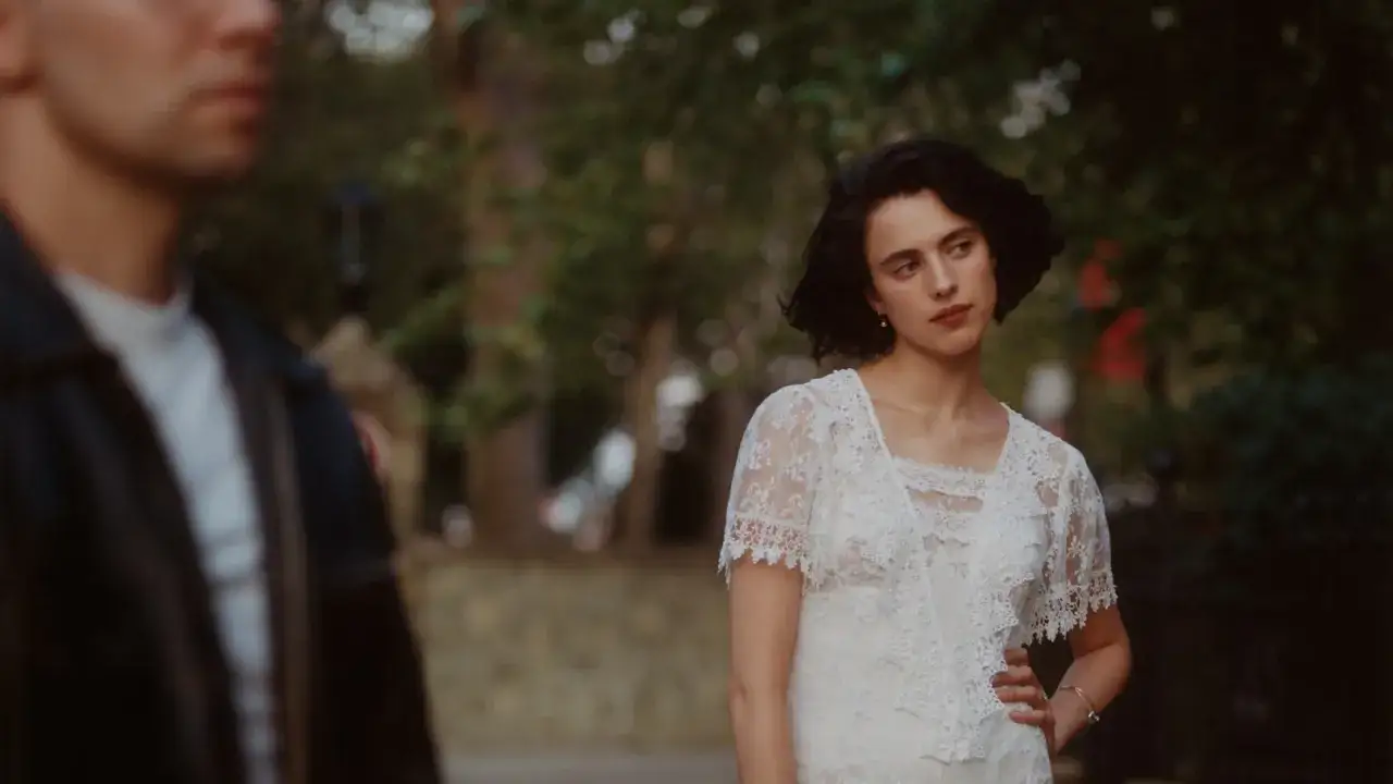 Kobieta w białej koronkowej sukni i mężczyzna w czarnej kurtce na tle drzew.