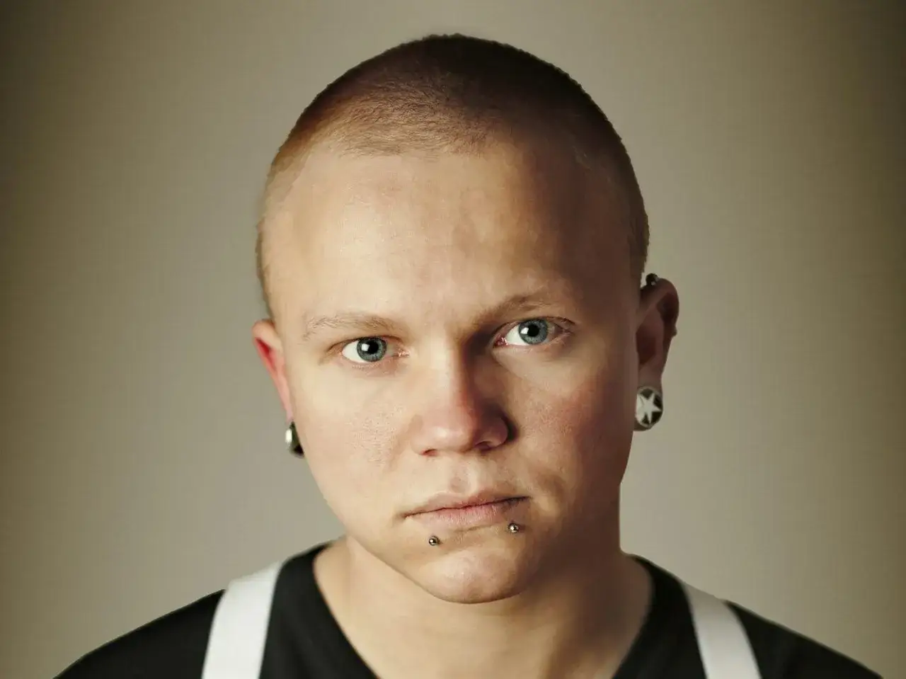 Mężczyzna z krótkimi włosami i kolczykami w uszach i ustach.