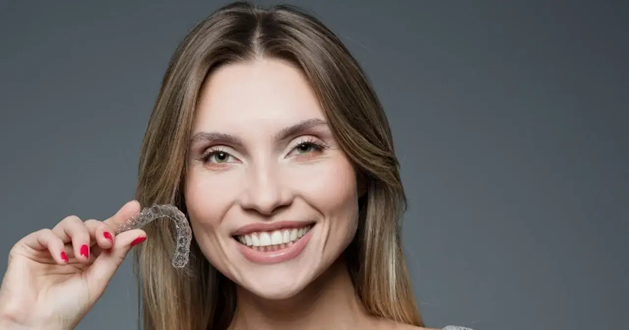 Uśmiechnięta kobieta pokazuje przezroczyste nakładki na zęby. Dowiedz się, ile kosztują nakładki na zęby.