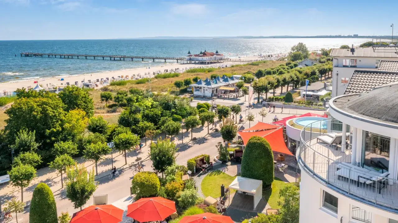 Blick auf Strandpromenade mit Seebrücke, Ostsee und Hotelterrasse mit Pool.