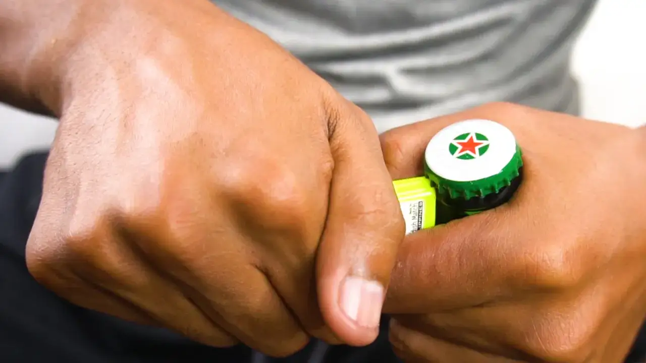 Dłonie otwierające butelkę piwa Heineken kluczem.