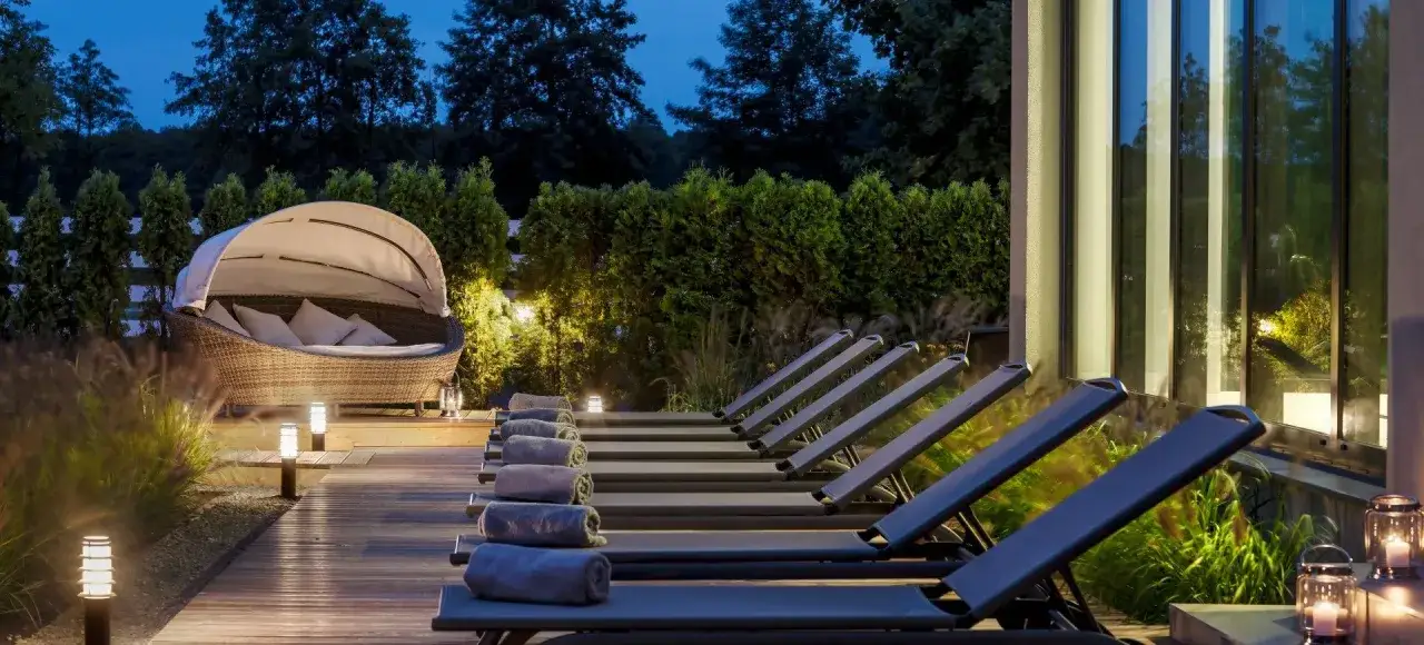 Leżaki i wiklinowa sofa z baldachimem na tarasie spa o zmierzchu.