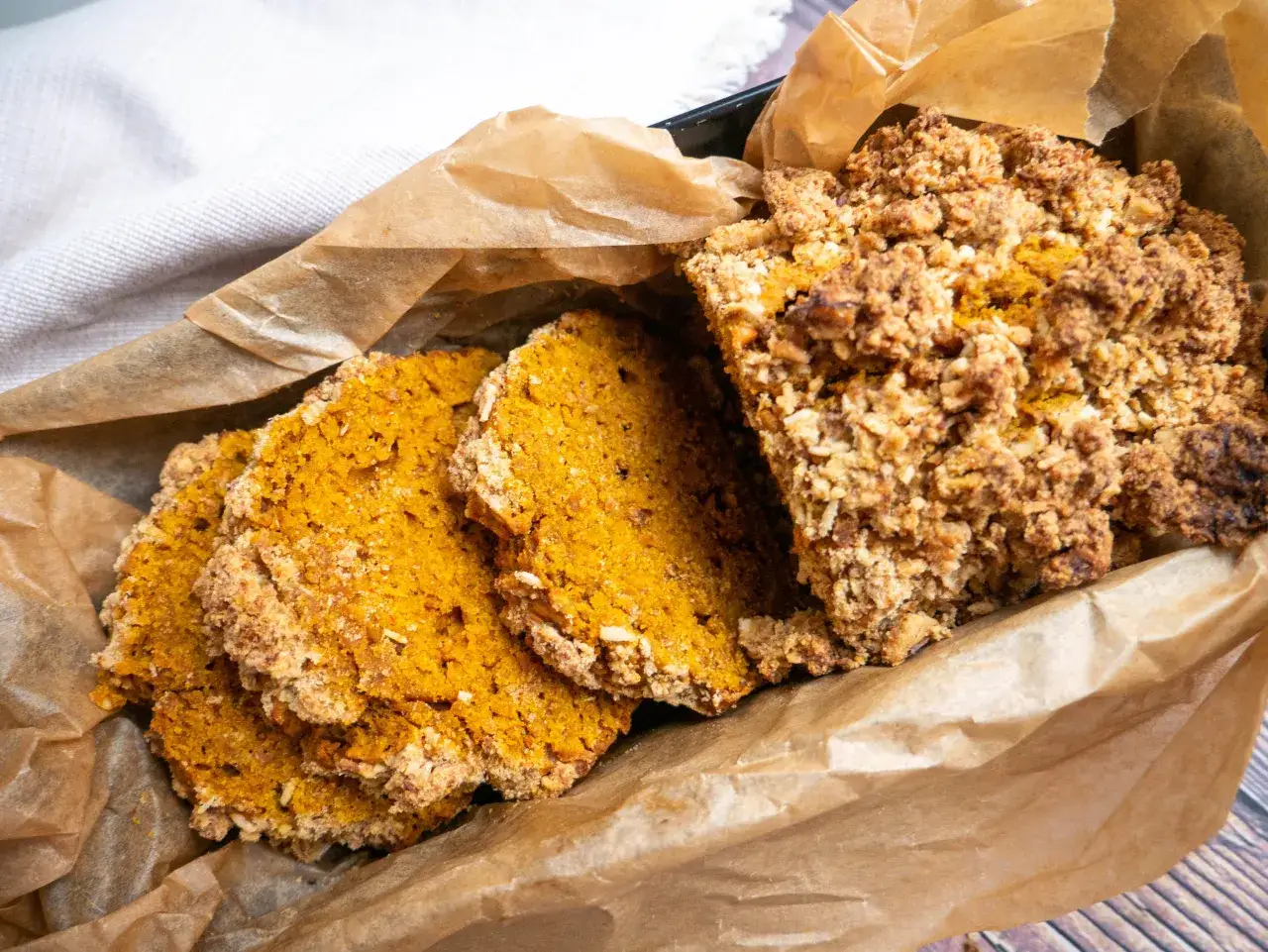 Okrasa łamie przepisy ciasto dyniowe z chrupiącą kruszonką, pokrojone na plastry, w papierze do pieczenia.