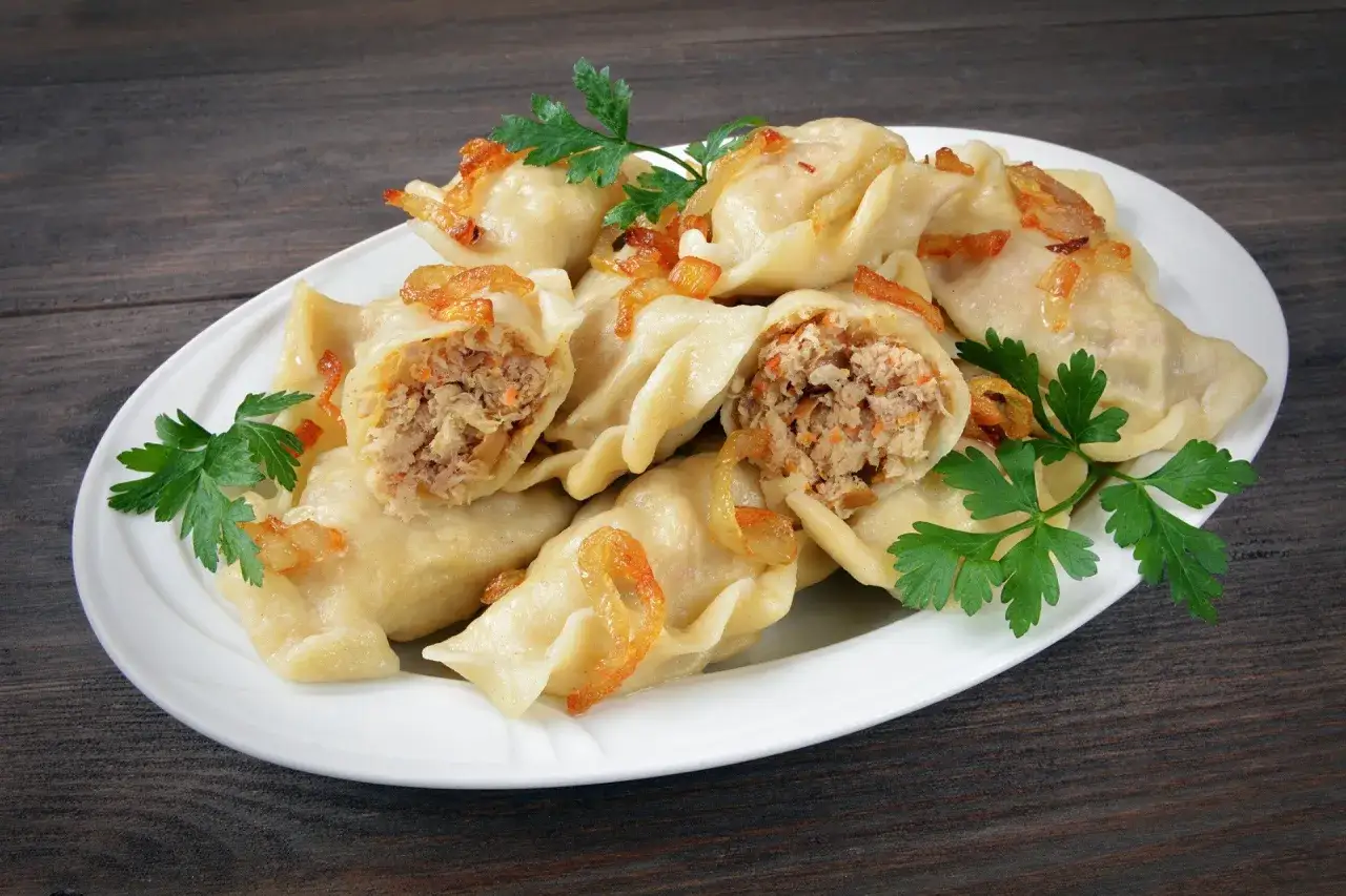 Pyszne pierogi z mięsem i kapustą, okraszone skwarkami i udekorowane natką pietruszki, na białym talerzu.