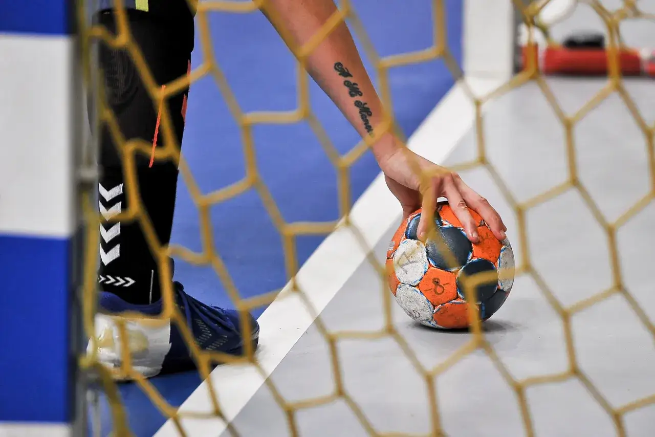 Piłka ręczna. Czy dogrywka trwa 5 minut? Zawodnik z tatuażem na ręce trzyma piłkę przy siatce bramki.