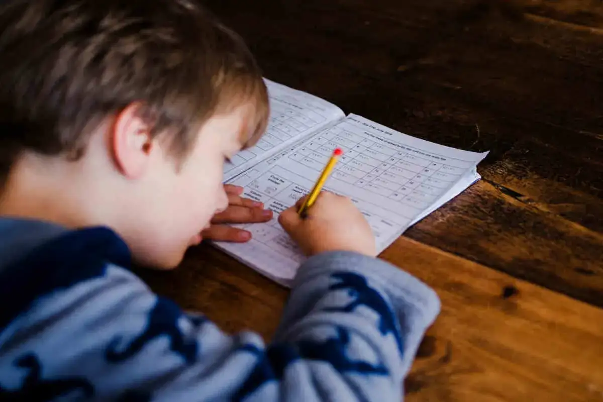 Chłopiec pisze w zeszycie w jedną linię, ćwicząc pisanie.
