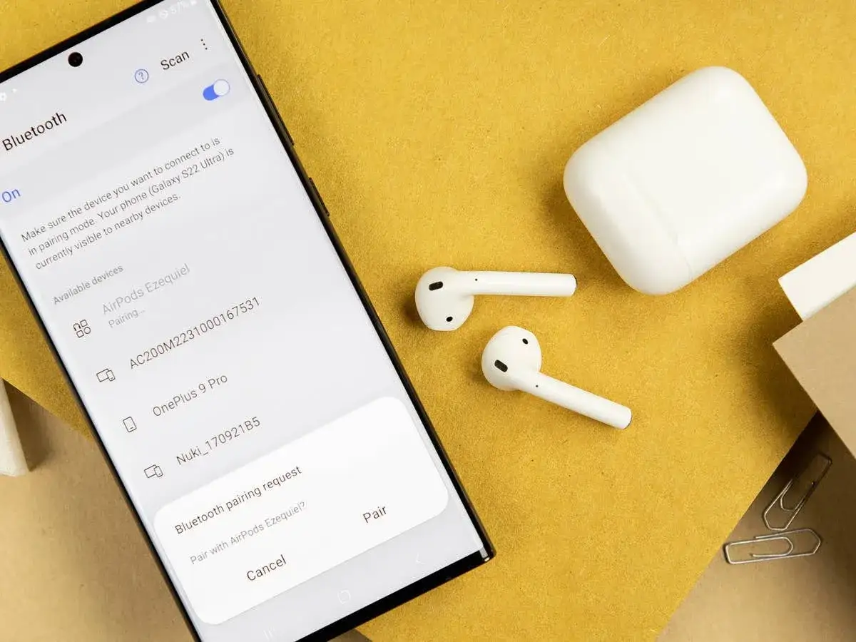 Samsung-Smartphone zeigt Bluetooth-Kopplungsanfrage für AirPods an, daneben liegen AirPods und Ladecase.