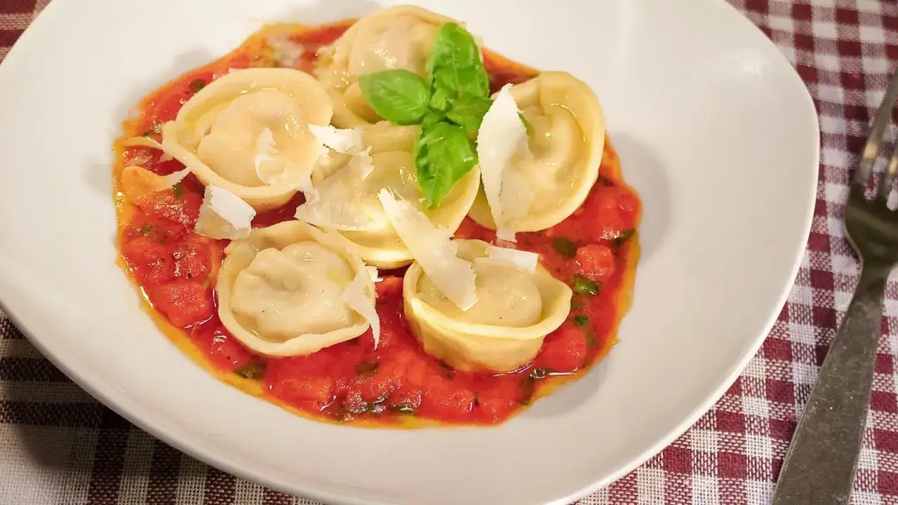 Tortellini z prosciutto w sosie pomidorowym, posypane parmezanem i udekorowane bazylią.