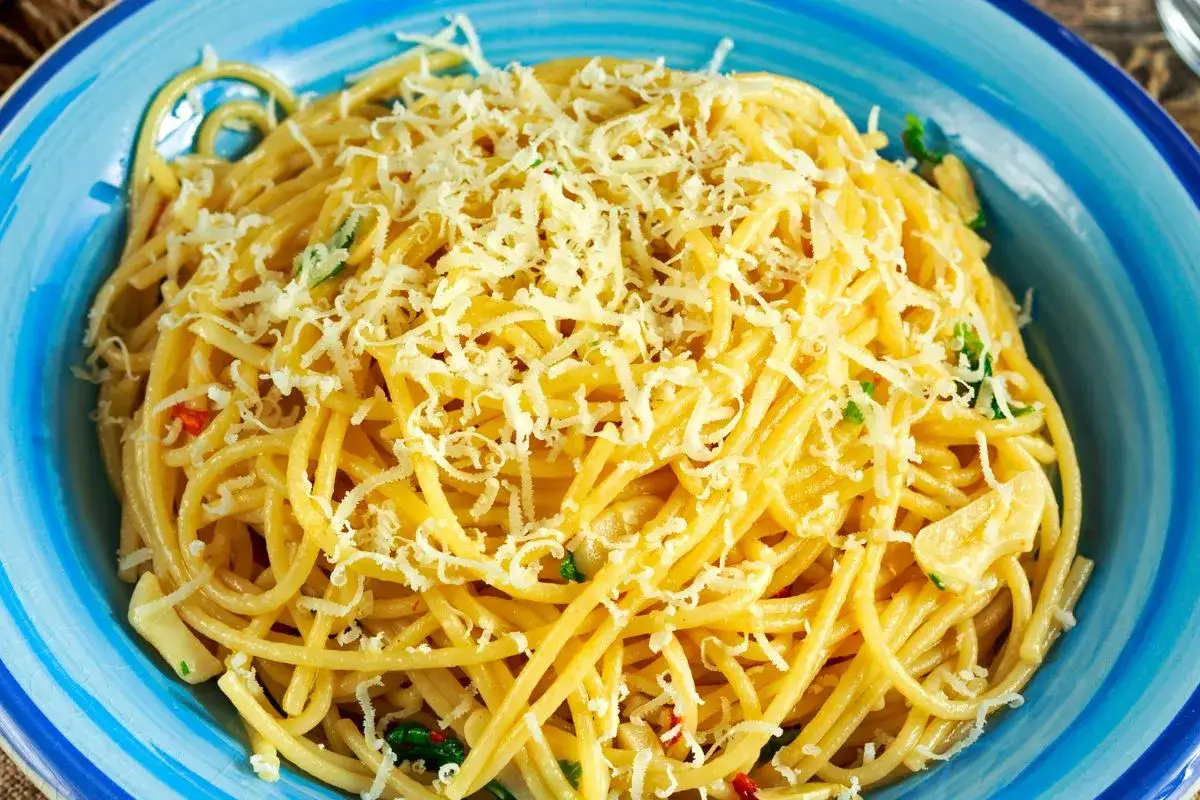 Porcja spaghetti z tartym serem i ziołami w niebieskiej misce.