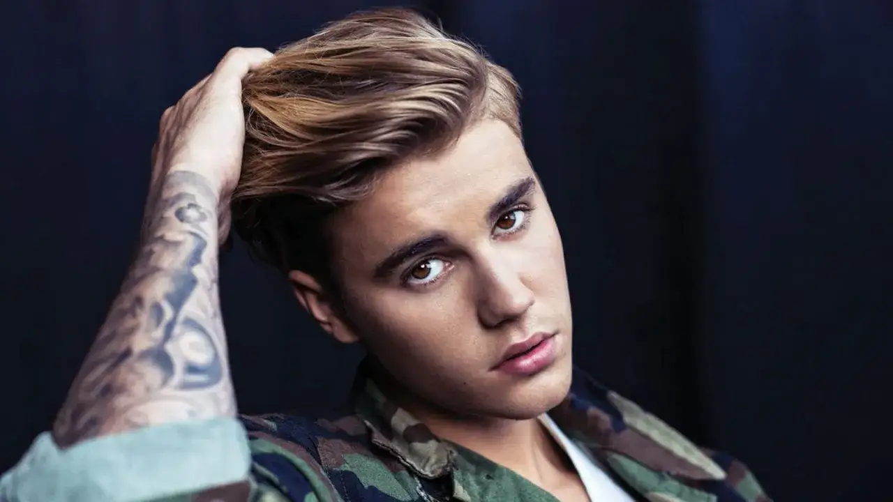 Justin Bieber mit tätowiertem Arm und Camouflage-Jacke, blickt in die Kamera.